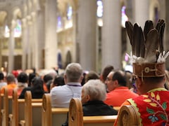 Un homme vêtu d'une coiffe à plumes assiste à la messe.