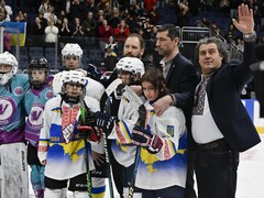 Des joueurs des deux équipes posent pour une photo. Un entraineur ukrainien envoie la main au public. 