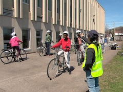 Au premier plan, une femme avec un dossard fait un signe à une jeune fille sur un vélo. Derrière, d'autres filles sont à vélo et attendent leur tour.