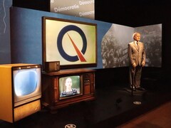 Une statue de René Lévesque en exposition avec deux vieux téléviseurs.