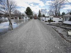 Une route de gravelle entre des maisons à Sainte-Marthe-sur-le-Lac, alors qu'on voit encore de l'eau d'un côté de la route.