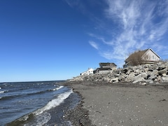 Des maison se trouvent près de la plage. Des roches les protègent de l'eau.