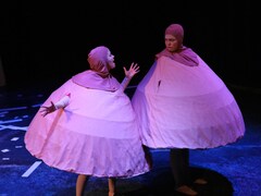 Sarah Bergbush et Bobbi Jones sur scène, habillées en seins géants. Elles portent un tissu rose pâle avec un mamelon sur leur tête. 