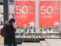 Une femme marchant dans la rue devant une vitrine affichant 50% de rabais