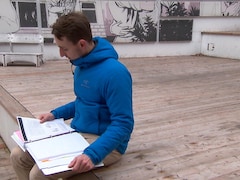 Un jeune homme ouvre un cartable rempli de notes, à l'extérieur. 