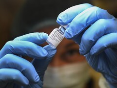 Une travailleuse de la santé vêtue d'équipements de protection personnelle tient dans ses mains une petite bouteille contenant une dose de vaccin.