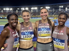 Quatre femmes se tiennent par la taille et sourient pour la caméra. Elles sont en bordure d'une piste d'athlétisme.
