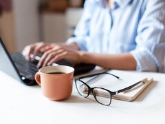 Une femme travaille sur un ordinateur portable. Une tasse de café et des lunettes se trouvent en avant-plan.