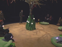 Spectateurs assis sur des coussins, en cercle autour d'un arbre décoratif.