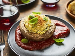 Un champignon portobello farci et gratiné, disposé sur une sauce tomate dans une assiette.