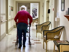 Une personne âgée se déplace en marchette dans le corridor d'une résidence privée pour aînés.