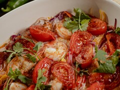 Un plat de service contenant des crustacés, des tomates, des poivrons et de la verdure.