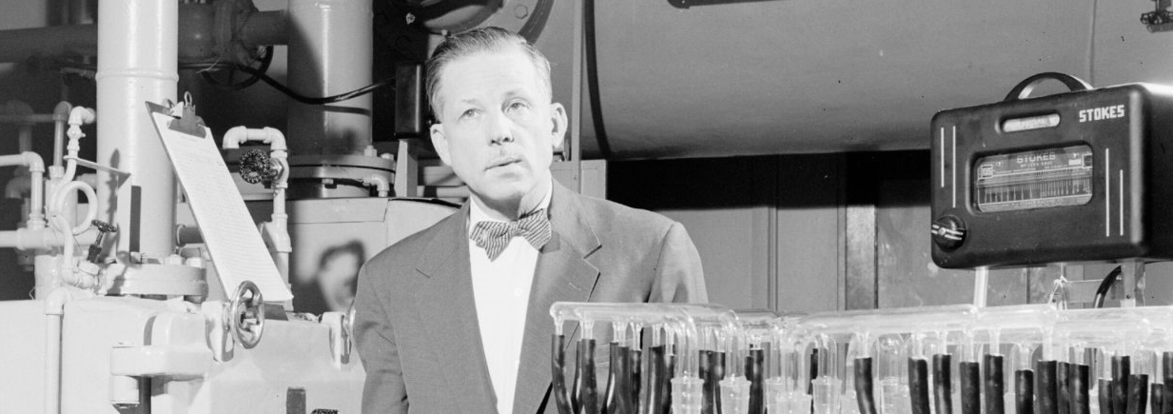 Le microbiologiste Armand Frappier se tient debout à côté d'équipements scientifiques.