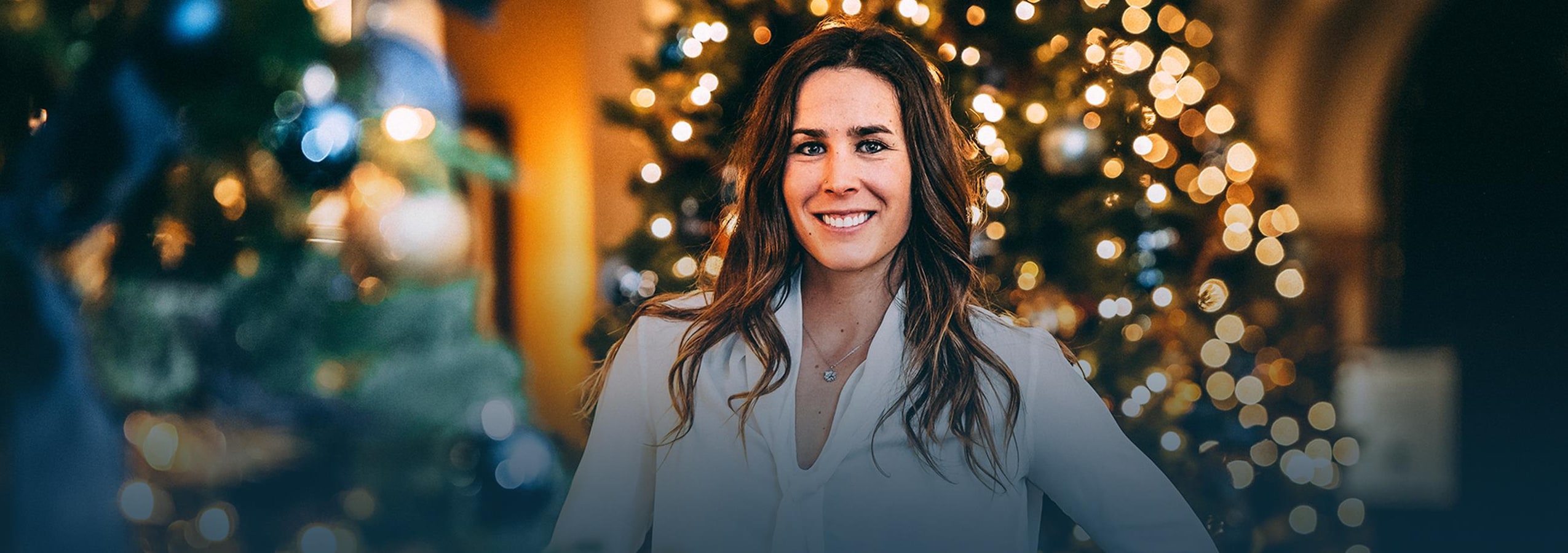 Marie-Michèle Gagnon - Lettre à ma famille pour Noël Debout entre deux sapins de Noël, Marie-Michèle Gagnon sourit.