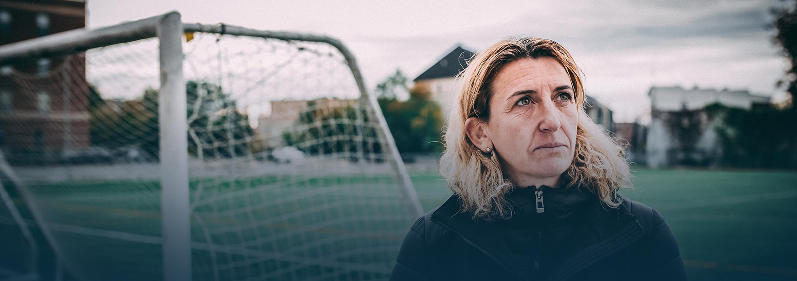 Marinette Pichon - Sauvée par le foot Marinette Pichon regarde au loin en se tenant devant un but de soccer.