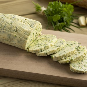Un bloc de beurre aux herbes est découpé sur une planche de bois.