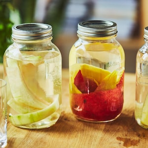 Trois pots Mason avec des retailles de melon, de mangue et d'ananas infusées dans de l'eau.