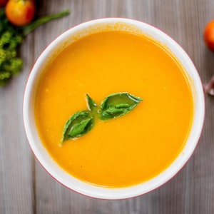 Un bol de soupe orange avec des feuilles de basilic.