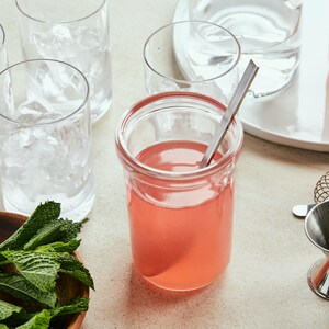 Petit pot de sirop de rhubarbe, menthe fraîche et ustensiles à cocktail.