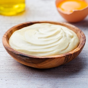 Un bol en bois rempli de mayonnaise avec une pincée de sel dans une cuillère.