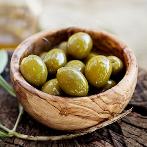 Un bol en bois rempli d'olives vertes, avec une branche d'olivier.