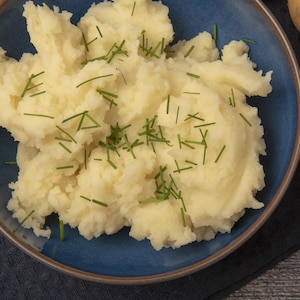Pommes de terre écrasées et ciboulette dans un bol, gousse d'ail et une patate.