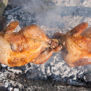 2 poulets entiers qui cuisent sur une broche au dessus d'une braise fumante.