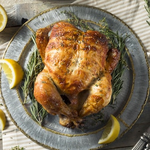 Poulet entier rôti dans une assiette avec des branches de romarin et quartiers de citron.