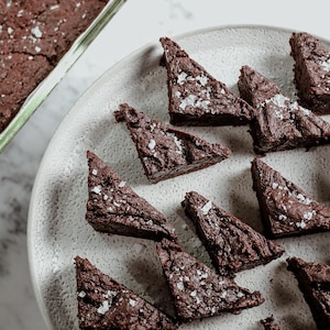 Une assiette de morceaux triangulaires de brownies, aux côtés d'une plaque de brownies.