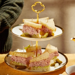 Plusieurs sandwichs au jambon coupés en triangles dans un joli présentoir servis avec du thé.