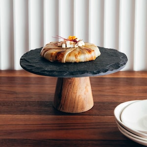 Une tarte Tatin garnie de cubes de fromage feta, sur un support à gâteau en ardoise et en bois.