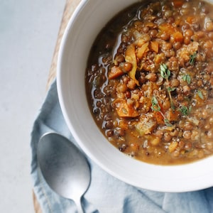 Vue en plongée d'un bol de soupe aux lentilles et légumes avec une cuillère posée à côté du bol.
