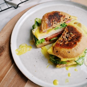 Un sandwich déjeuner végétalien coupé en deux dans un assiette posée sur une planche en bois.