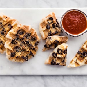 Quelques focaccias aux olives sur une planche avec un pot de sauce tomate