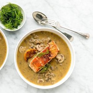 Deux bols de soupe remplis de soupe veloutée aux champignons avec du saumon poêlé sur le dessus.