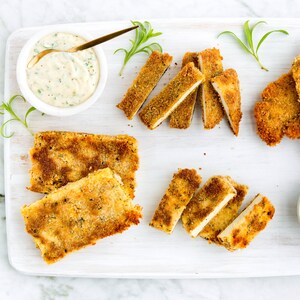Des tranches de tofu et de poulet panées disposées sur une planche à découper. Servi avec de la mayonnaise et des quartiers de citron.
