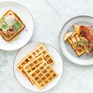 Quatre gaufres dans une assiette, deux assiettes avec une gaufre garnie et une assiette de garniture.