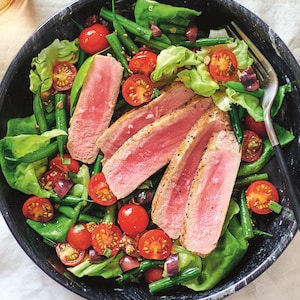 Des tranches de thon frais sur une salade verte composée de haricots verts, de tomates cerises, ainsi que des feuilles de laitue Boston.