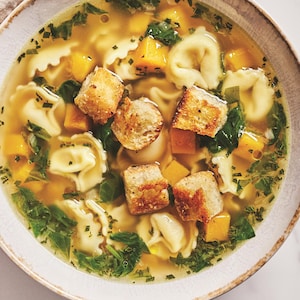 Un bol de soupe-repas contenant des tortellinis au fromage, des dés de courge et des croûtons de pain.