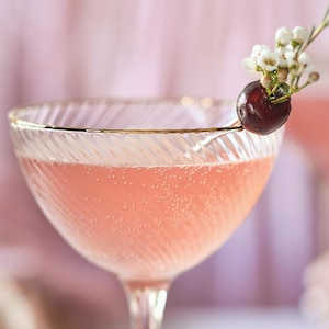 Un cocktail au jasmin et à la cerise décoré d'une cerise et de petites fleurs.