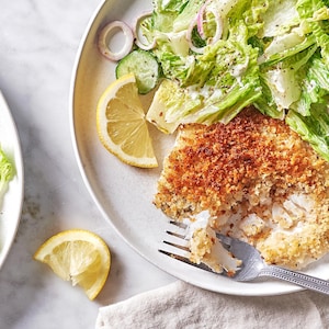 Un morceau d'aiglefin pané et frit dans une assiette accompagné d'une salade verte.