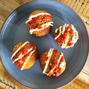 Dans une assiette, il y a quatre croquettes frites avec de la sauce mayonnaise, du ketchup et des graines de caméline en garniture. 
