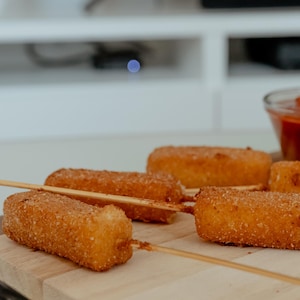 Des bâtonnets de fromage frits sur une planche de service avec un bol de sauce.