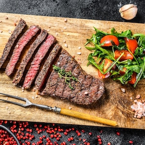 Une bavette de bœuf et une salade sur une planche à découper.
