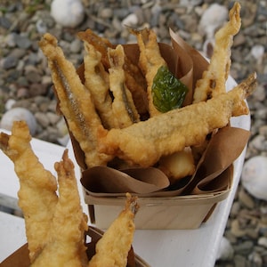 Des beignets d'éperlans frits servis dans un cône en papier comme des frites.