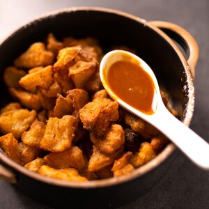 Des morceaux de beignets de pommes frites dans une plat en terre cuite muni de deux anses, et une cuillère en céramique de caramel posée sur le dessus.