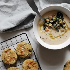 Un bol de soupe crémeuse à côté de biscuits salés avoine et pois chiches sur une grille de refroidissement.