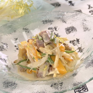 Une petite salade colorée de jaune, de vert pâle et de blanc, recouverte d'une vinaigrette crème, dans une assiette transparente.