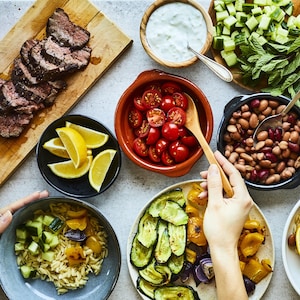 Tablée avec des bol-repas à assembler : choix de boeuf, tomates, courgettes, orzo, tzatziki, etc.