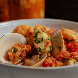 Des fruits de mer variés (palourdes, poissons) baignant dans un bouillon de sauce tomates, servis dans un bol. 